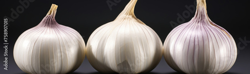 Three garlic are placed in a row against a black background. The garlic is white and has a papery outer skin.