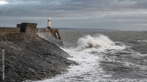 Rough seas and waves crashing into a sea wall and lighthouse (Porthcawl, South Wales, UK) on a cloudy, winters day