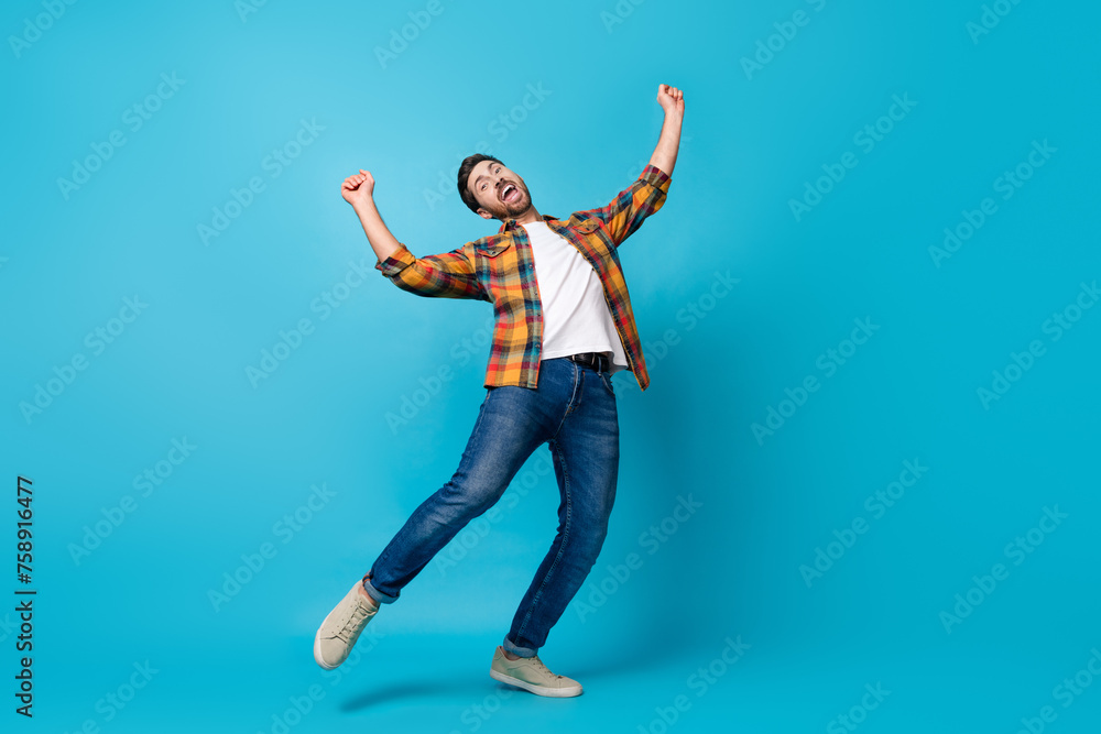 Full body photo of attractive young man dancing raise fists celebrate wear trendy plaid clothes isolated on blue color background