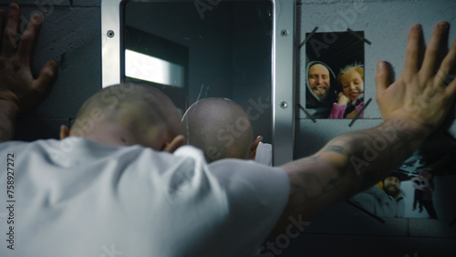 Illegally convicted man looks at himself in the mirror, puts hand on the pictures with family hanging on the wall in prison cell. Male prisoner serves imprisonment term in jail or detention center.
