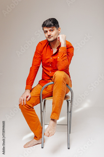 Man in bright orange clothes sits on a chair and looks at the camera