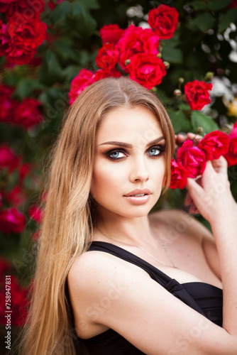 Beautiful fashionable woman with red lips makeup posing outdoor, in blooming rose garden.