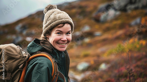 A woman with a hat and backpack on a mountain trail smiles happily © Anoo