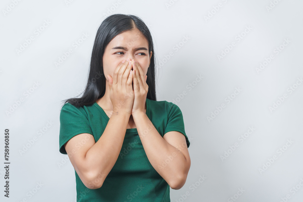 Young Asian frustrated woman with green t-shirt pinches her nose with disgust on her face, reacting to a bad smell in isolation over background. Young Asian frustrated woman with green t-shirt pinches her nose with disgust on her face, reacting to a bad smell in isolation over background.