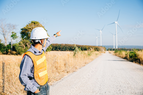 Technician in hardhat inspects windmill farm for clean energy. An Asian engineer ensures turbine efficiency showcasing innovation in global electricity development and growth. Expertise in service.