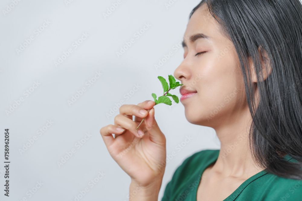 Beautiful young Asian woman in green t-shirt inhaling the aroma of herbal mint isolated on white background. Beautiful young Asian woman in green t-shirt inhaling the aroma of herbal mint isolated on white background.