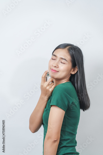 Beautiful young Asian woman in green t-shirt smells the aroma of perfume isolated on white background.