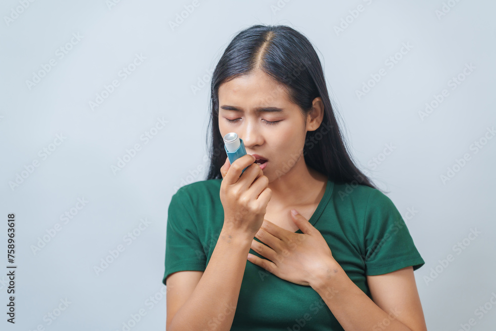 Young Asian woman wearing green t-shirt using asthma inhaler isolated on white background, indoors, studio shot. Young Asian woman wearing green t-shirt using asthma inhaler isolated on white background, indoors, studio shot.