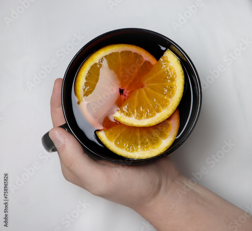 hot tea with oranges from which it is smoking in a black mug on a white background © Marie