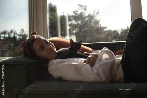 A young girl hugs a black cat on the coach at home. Cozy