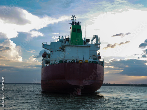 The stern of a merchant ship parked in Marajó Bay, in the state of Pará, Brazil. Export logistic trade industry of cargo transport loading in the sea with crimson cloud sky background.