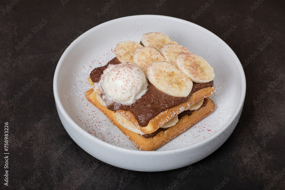 Belgian waffles with banana and chocolate sauce on a dark background