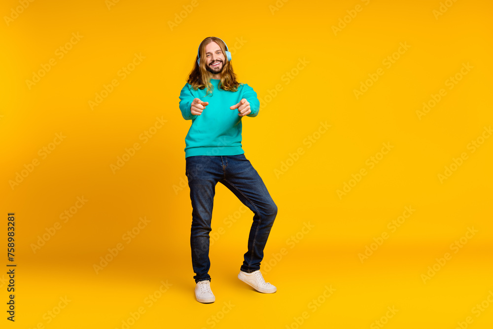 Full body portrait of positive nice man enjoy music headphones point fingers you empty space isolated on yellow color background Full body portrait of positive nice man enjoy music headphones point fingers you empty space isolated on yellow color background