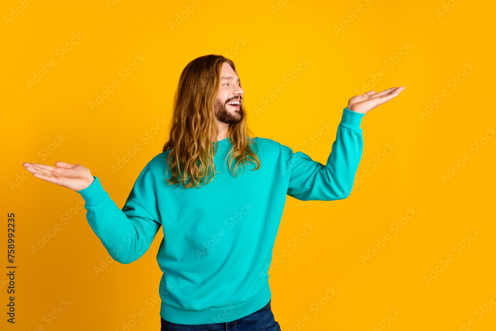 Portrait of positive guy look hands hold empty space proposition weighing isolated on yellow color background