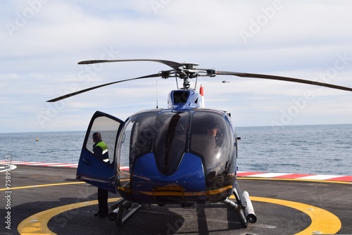 The helicopter sits on the helipad amidst the sea, its rotor blades poised for flight, a symbol of modern transportation and access to remote destinations.