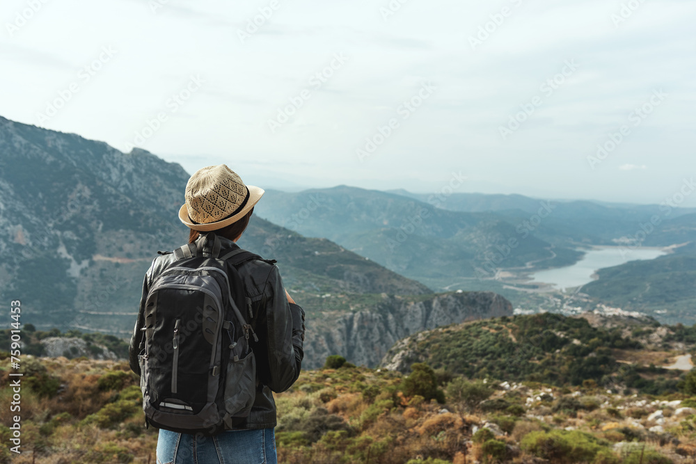 Woman traveler with a hat standing on a background of green mountains.