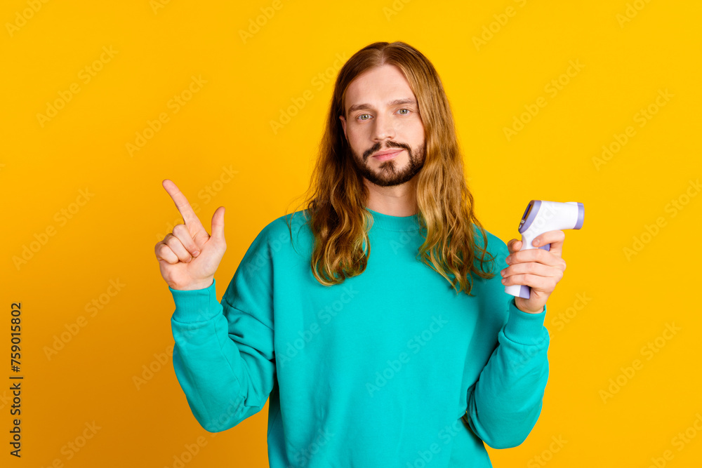 Portrait of attractive guy hold thermometer indicate finger empty space isolated on yellow color background