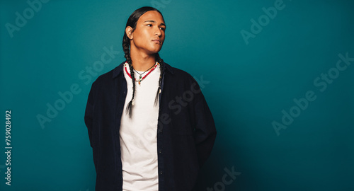 Native American man with braided hair and cultural jewelry standing in a studio