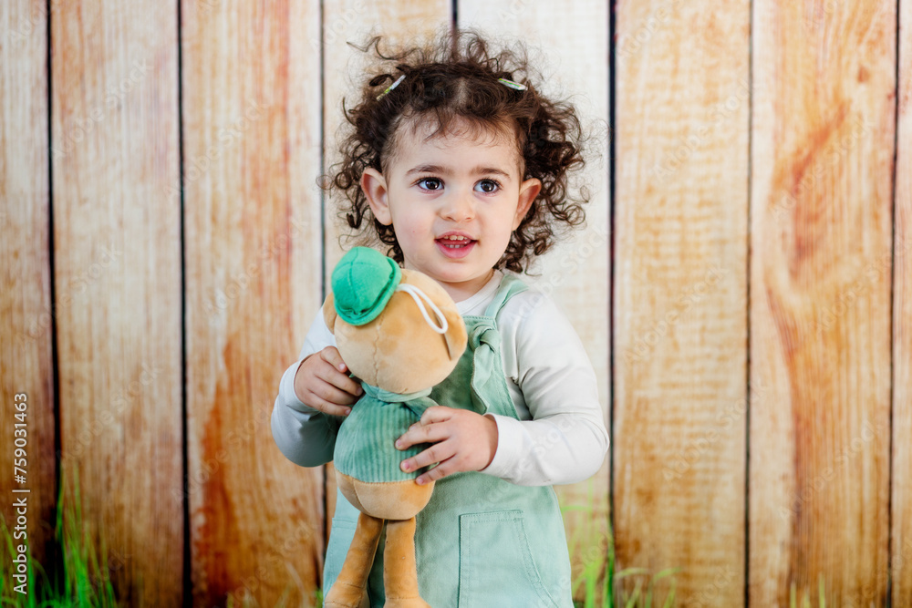 A curly hair girl s hands wrapped around a plush friend, showcasing a loving bond in front of rustic wooden setting