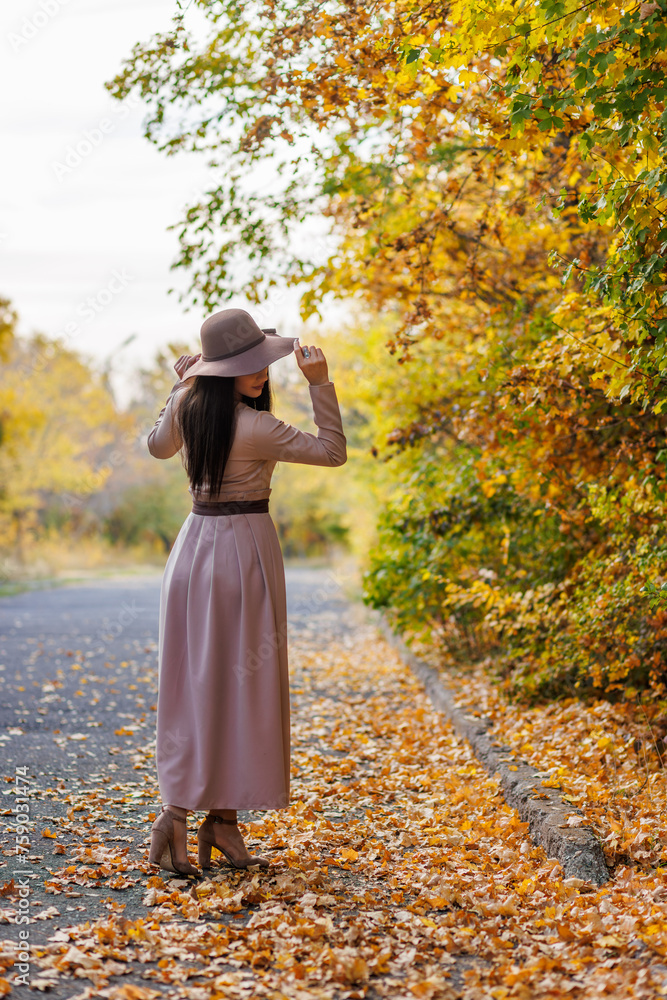 A leisurely walk through the autumn park. Young woman touching her wide - brimmed hat