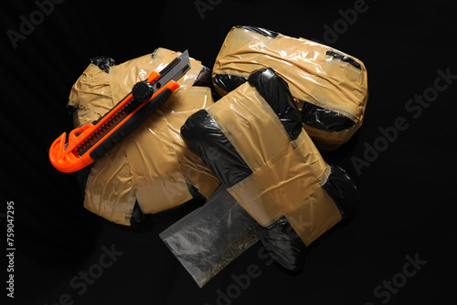 Smuggling, drug trafficking. Packages with narcotics and utility knife on black surface, flat lay photo