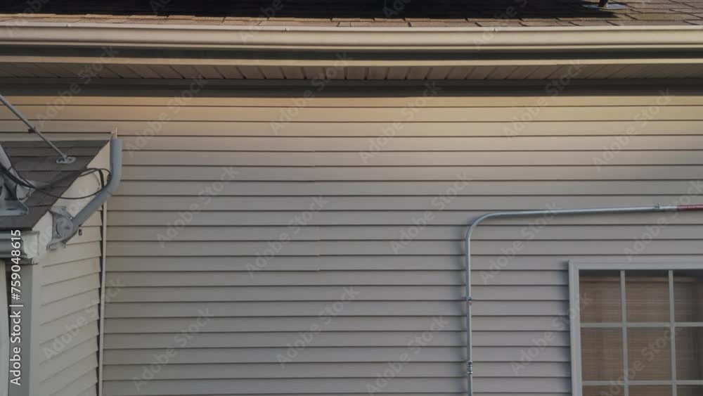 Exposed rooftop solar panels extend from the electrical boxes and inverter equipment attached to the exterior wall of a residential home. Exposed rooftop solar panels extend from the electrical boxes and inverter equipment attached to the exterior wall of a residential home.