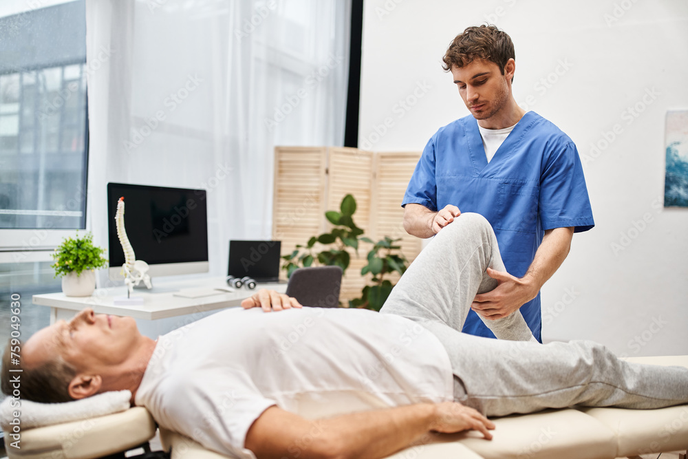 good looking doctor in blue robe helping his mature patient to stretch during rehabilitation good looking doctor in blue robe helping his mature patient to stretch during rehabilitation