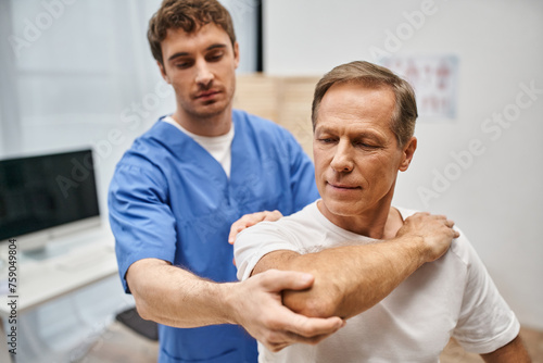 good looking patient in casual attire stretching his muscles with help of his handsome doctor