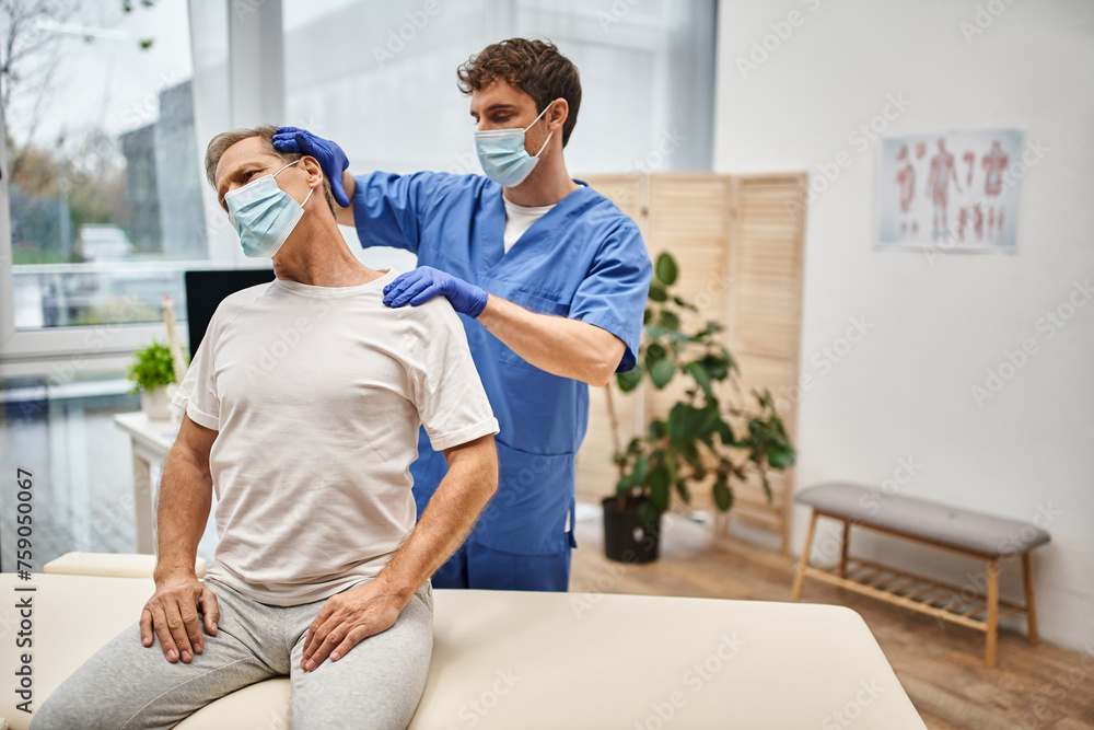 devoted doctor with mask and gloves helping his patient to stretch his body, rehabilitation devoted doctor with mask and gloves helping his patient to stretch his body, rehabilitation