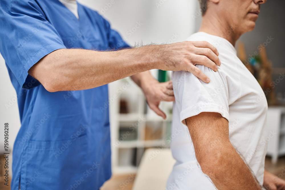 Obraz premium cropped view of dedicated doctor in blue robe helping his mature patient to rehabilitate in ward