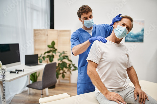 good looking dedicated doctor with mask and gloves stretching his mature patient on rehabilitation