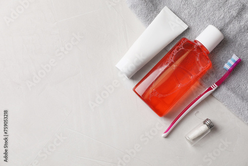 Fresh mouthwash in bottle, toothpaste, toothbrush and dental floss on light textured background, flat lay. Space for text