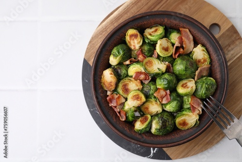 Delicious roasted Brussels sprouts and bacon in bowl on white table, top view. Space for text