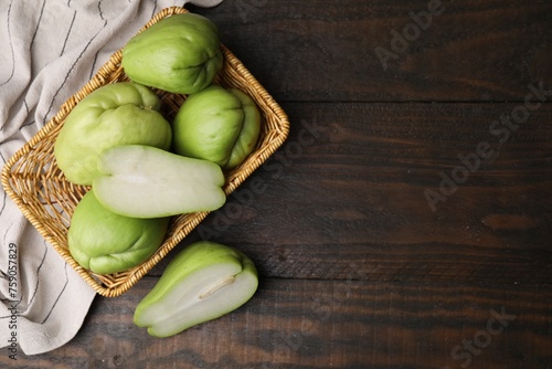 Cut and whole chayote in wicker basket on wooden table, flat lay. Space for text