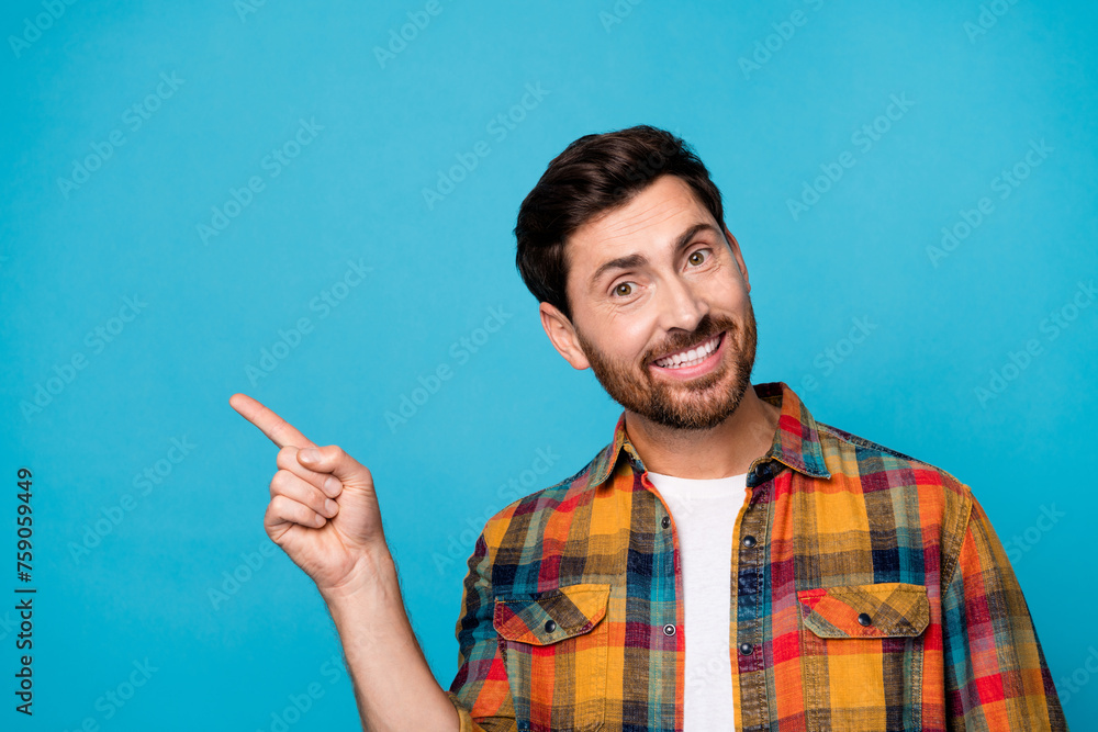 Fototapeta premium Photo of good mood pleasant man with beard dressed plaid shirt indicating at discount empty space isolated on blue color background