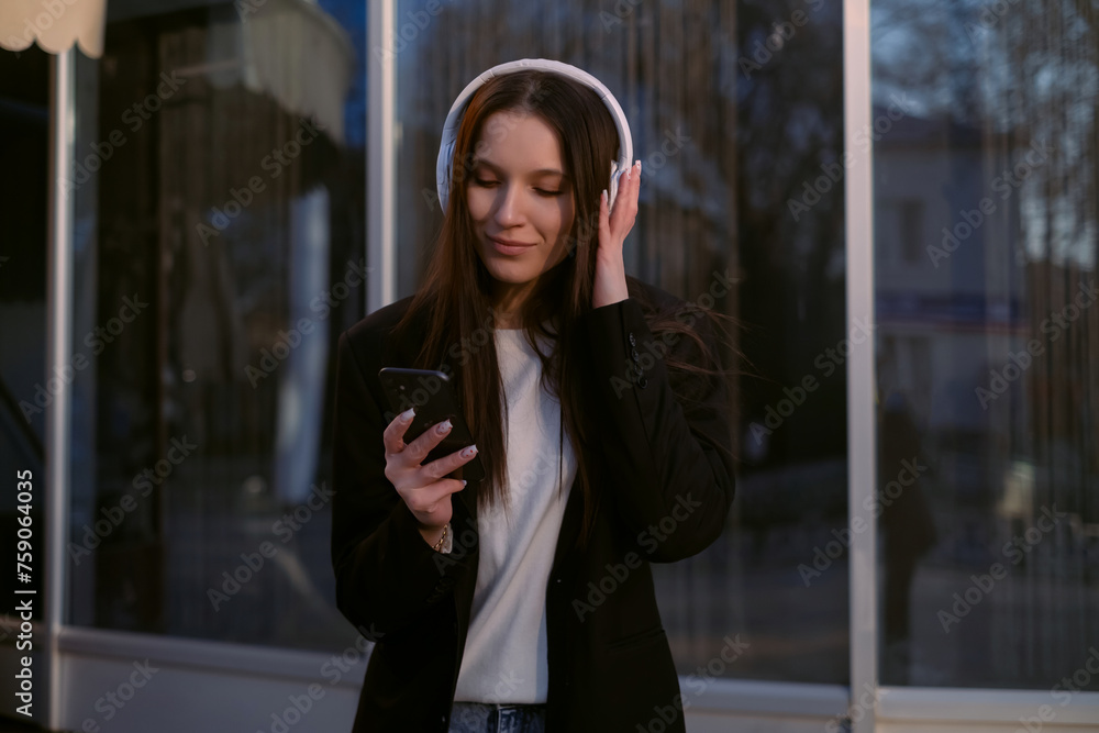 Fototapeta premium A woman in a suit and headphones dances cheerfully on the street, singing along to music, embodying joy and positivity. A freelancer enjoys the freedom of flexible work hours.
