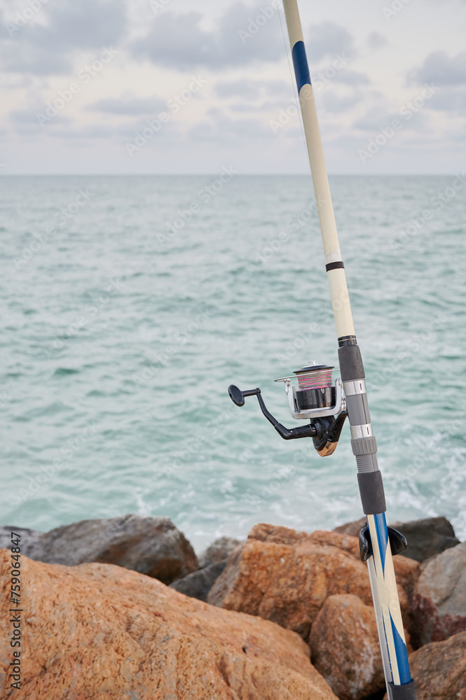 Close up view of a fishing rod and its reel of line placed on the breakwater waiting for the fish to bite. Tourism in the Mediterranean Sea. Close up view of a fishing rod and its reel of line placed on the breakwater waiting for the fish to bite. Tourism in the Mediterranean Sea.