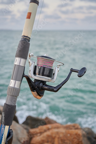 Close up view of a fishing rod and its reel of line placed on the breakwater waiting for the fish to bite. Tourism in the Mediterranean seaside.
