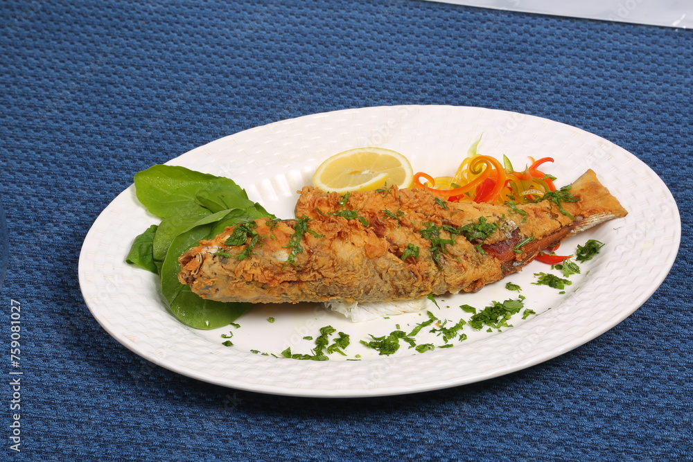 fish whole deep fry flour covered garnished with Arab vegetable white plate blue table fish whole deep fry flour covered garnished with Arab vegetable white plate blue table