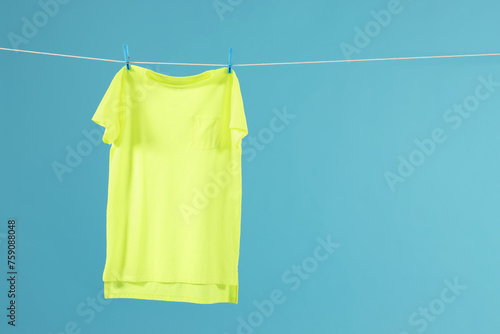 One green t-shirt drying on washing line against light blue background. Space for text
