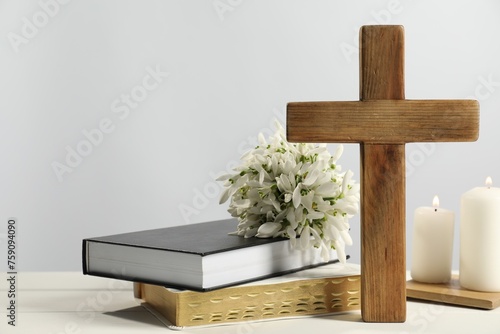 Burning church candles, wooden cross, ecclesiastical books and flowers on white table. Space for text photo