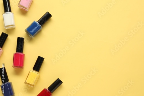 Bright nail polishes in bottles on yellow background, flat lay. Space for text