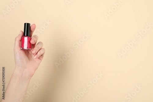 Woman holding nail polish on beige background, closeup. Space for text