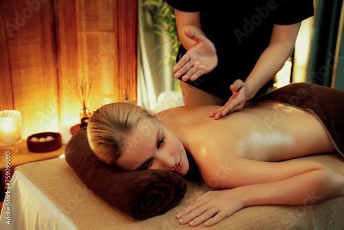 Caucasian woman customer enjoying relaxing anti-stress spa massage and pampering with beauty skin recreation leisure in warm candle lighting ambient salon spa at luxury resort or hotel. Quiescent