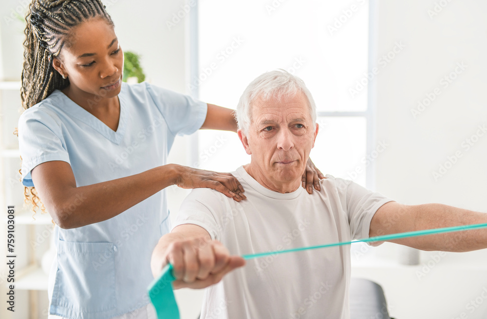 Black physiotherapist helping senior man with in clinic. Elderly man undergoing physiotherapy treatment for injury Black physiotherapist helping senior man with in clinic. Elderly man undergoing physiotherapy treatment for injury