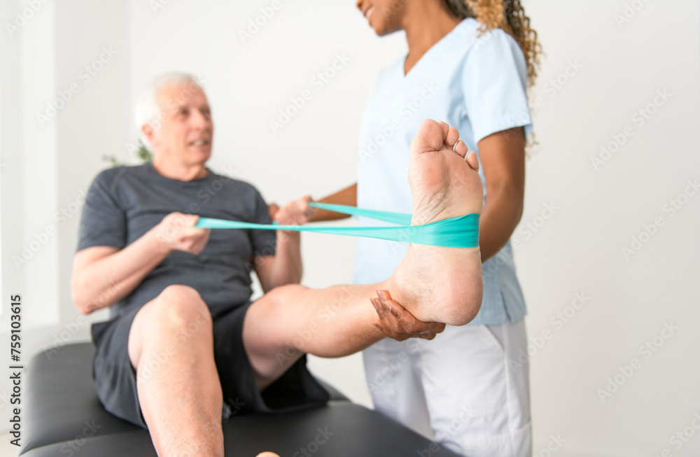 Fototapeta premium Black physiotherapist helping senior man with in clinic. Elderly man undergoing physiotherapy treatment for injury