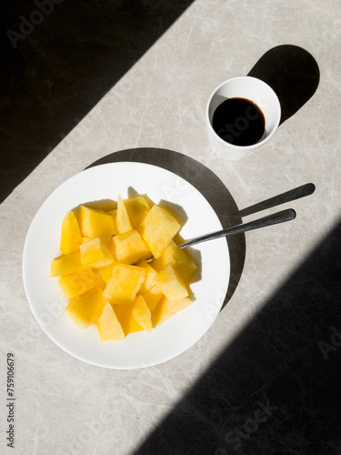 A plate with yellow fruit and a cup of black coffee