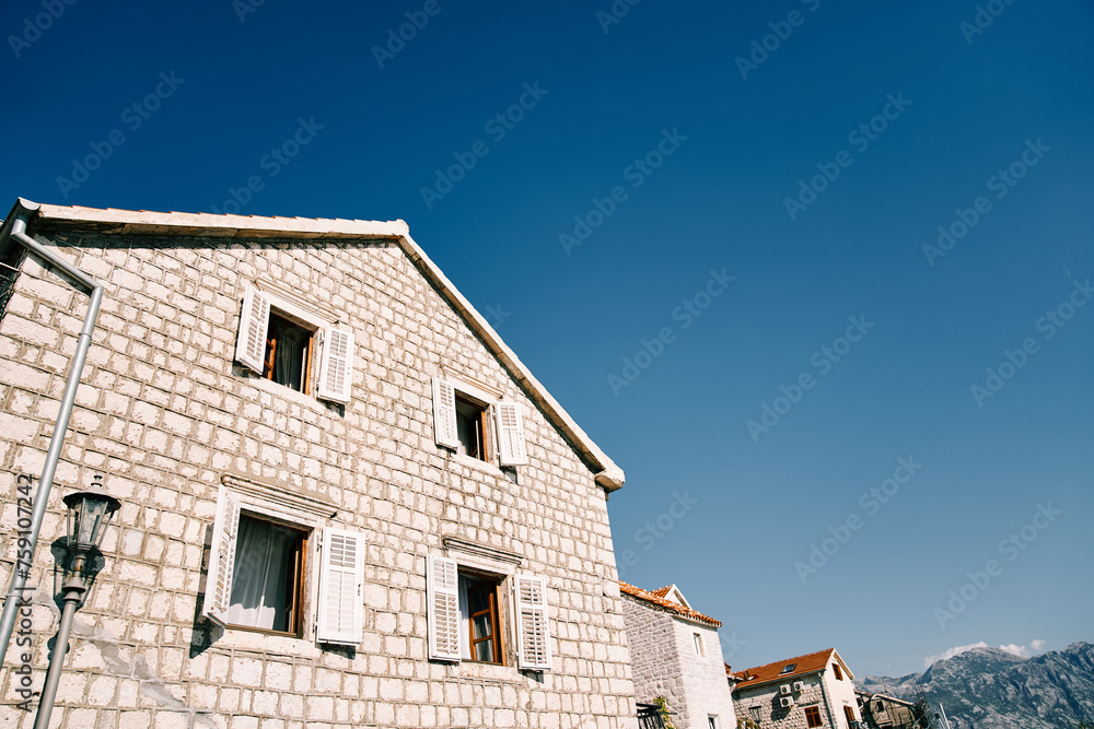 Ancient stone house with white wooden open shutters against a blue sky