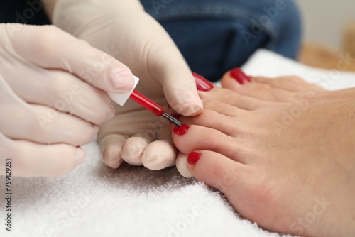 Pedicurist painting client s toenails with red polish in beauty salon  closeup