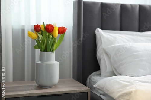 Beautiful tulips in vase on bedside table indoors